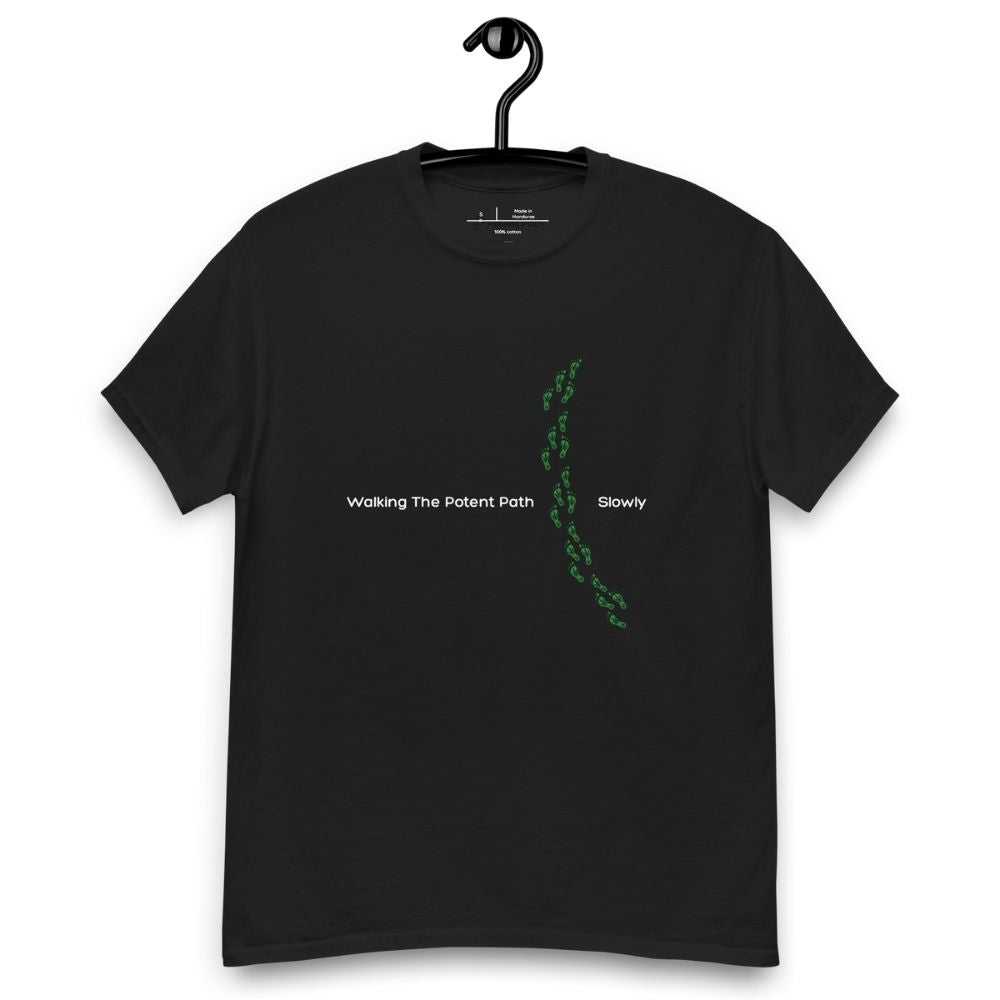 Black t-shirt on a hanger featuring the phrase "Walking The Potent Path Slowly" in white text across the chest, with a vertical trail of small green footprints with cannabis leaves inside between "Path" and "Slowly"