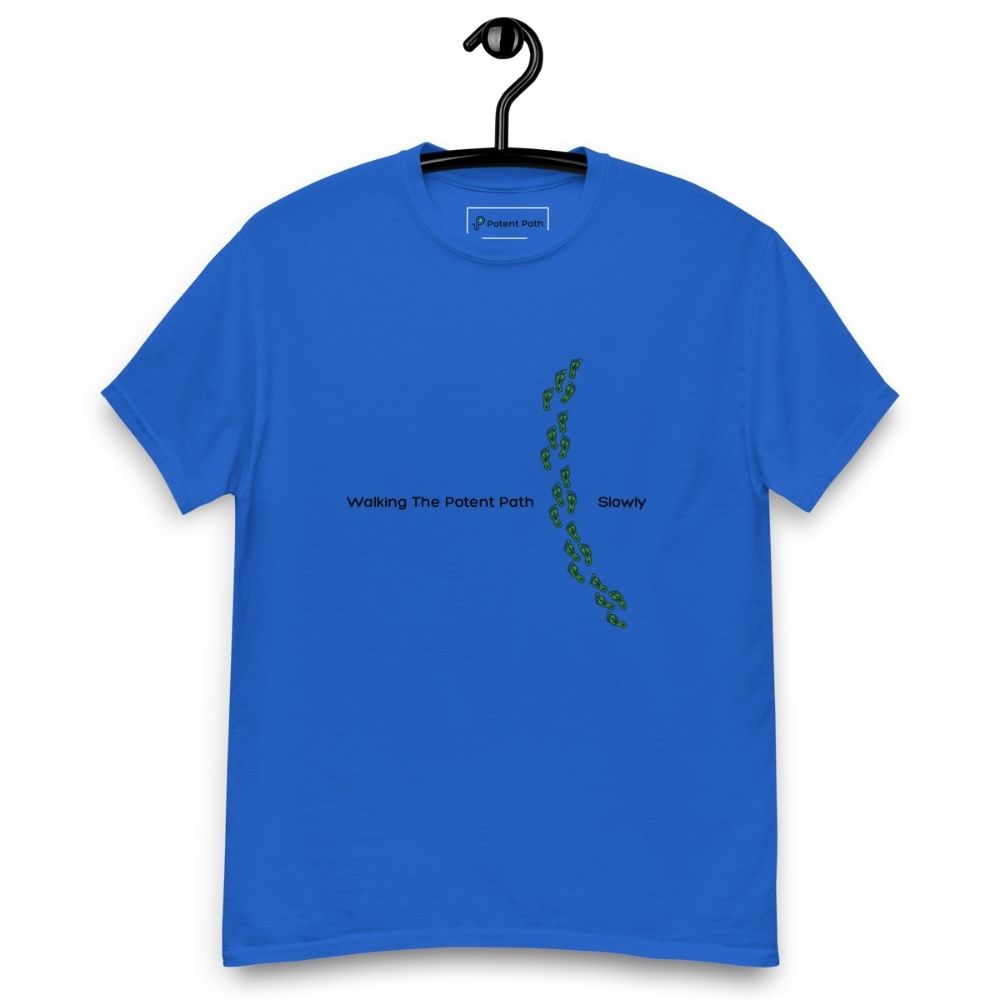 Blue t-shirt on a hanger featuring the phrase "Walking The Potent Path Slowly" in white text across the chest, with a vertical trail of small green footprints with cannabis leaves inside between "Path" and "Slowly"