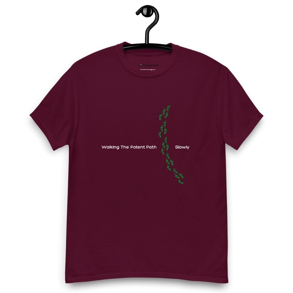 Burgundy t-shirt on a hanger featuring the phrase "Walking The Potent Path Slowly" in white text across the chest, with a vertical trail of small green footprints with cannabis leaves inside between "Path" and "Slowly"