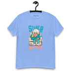 Caroline blue T-shirt on a hanger featuring a cartoon illustration of an elderly woman in a teal tracksuit sitting in an armchair, holding a yellow bong, with the text "STONER GRANNY" above and below her.
