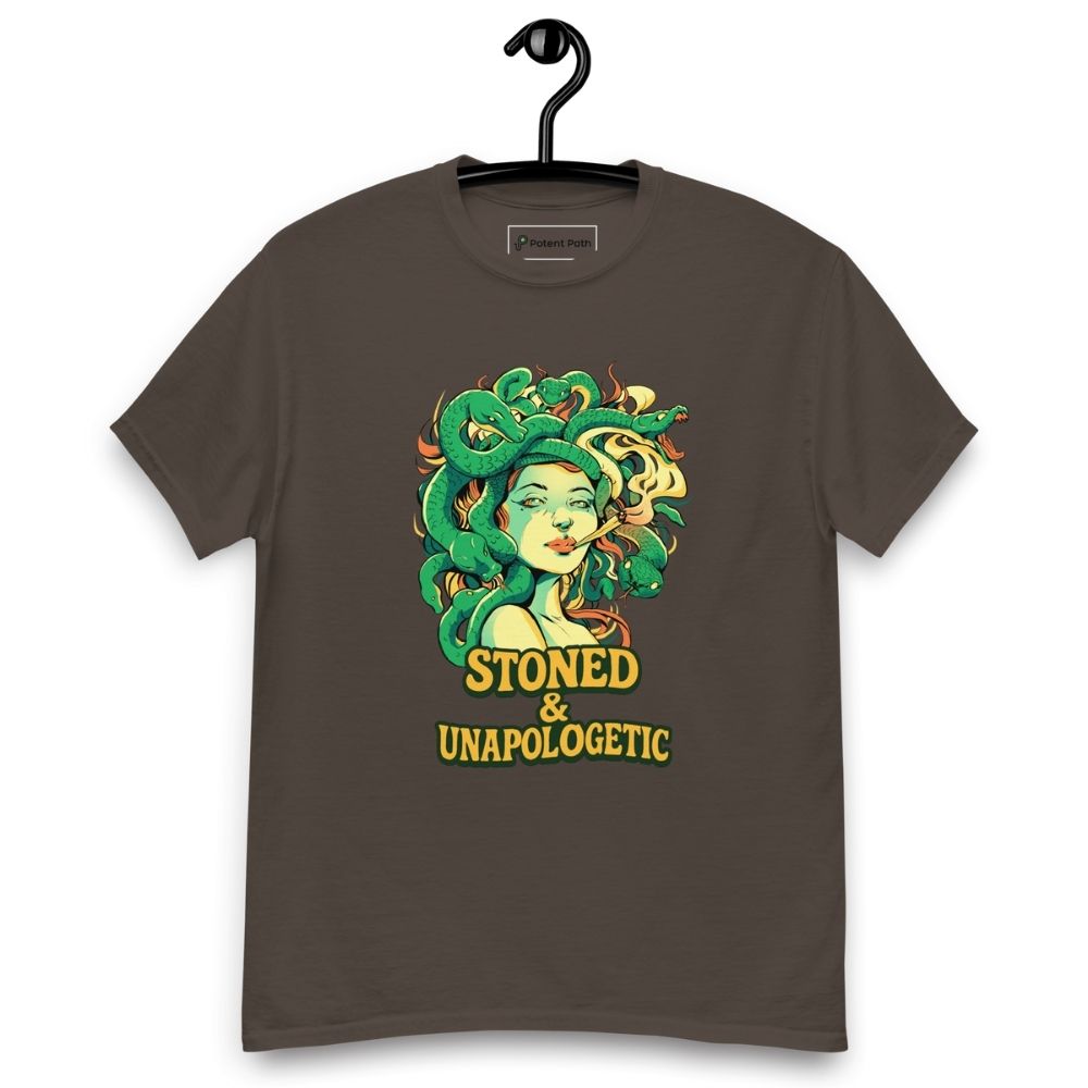 Dark chocolate T-shirt on a hanger featuring a Medusa head smoking a joint with green snake hair, and the text "STONED & UNAPOLOGETIC" below