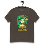 Dark chocolate T-shirt on a hanger featuring a Medusa head smoking a joint with green snake hair, and the text "STONED & UNAPOLOGETIC" below