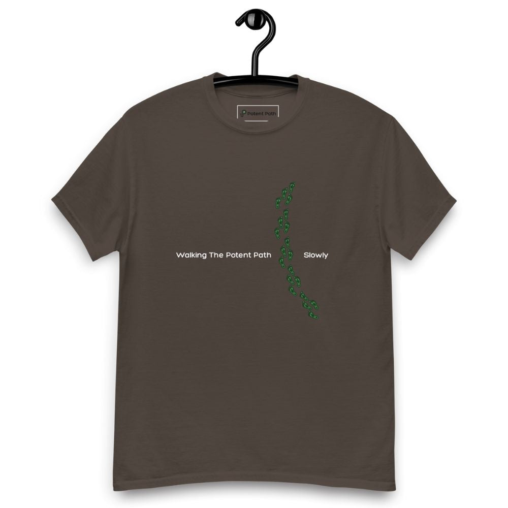 Dark chocolate colour t-shirt on a hanger featuring the phrase "Walking The Potent Path Slowly" in white text across the chest, with a vertical trail of small green footprints with cannabis leaves inside between "Path" and "Slowly"
