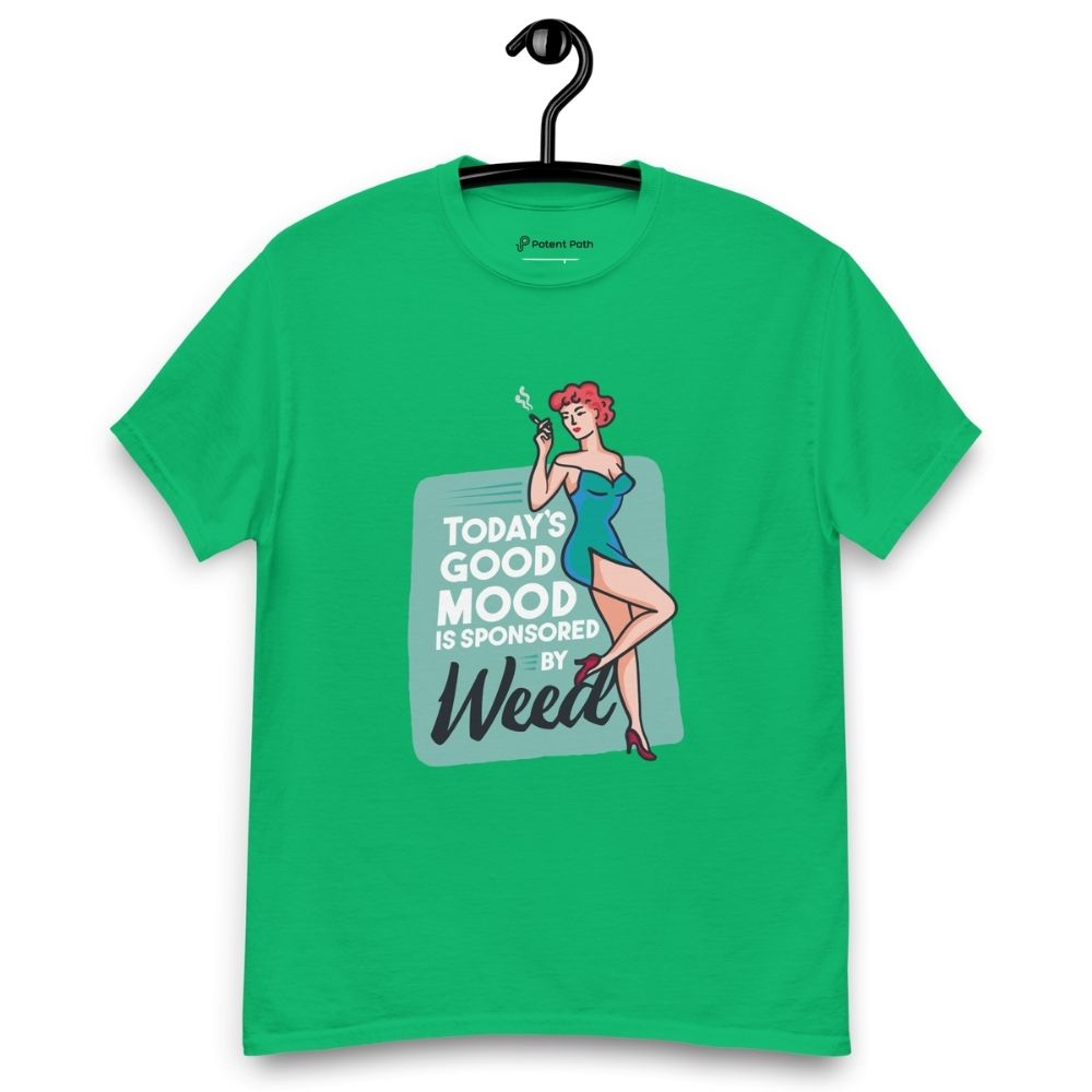 Green T-shirt on a hanger featuring a retro-style illustration of a woman in a teal dress holding a smoking joint, next to the text “TODAY'S GOOD MOOD IS SPONSORED BY Weed"