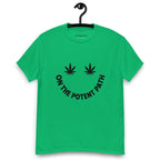 Green t-shirt on a hanger featuring curved text reading "ON THE POTENT PATH" in the form of a smiley face and two black cannabis leaves above to represent the eyes
