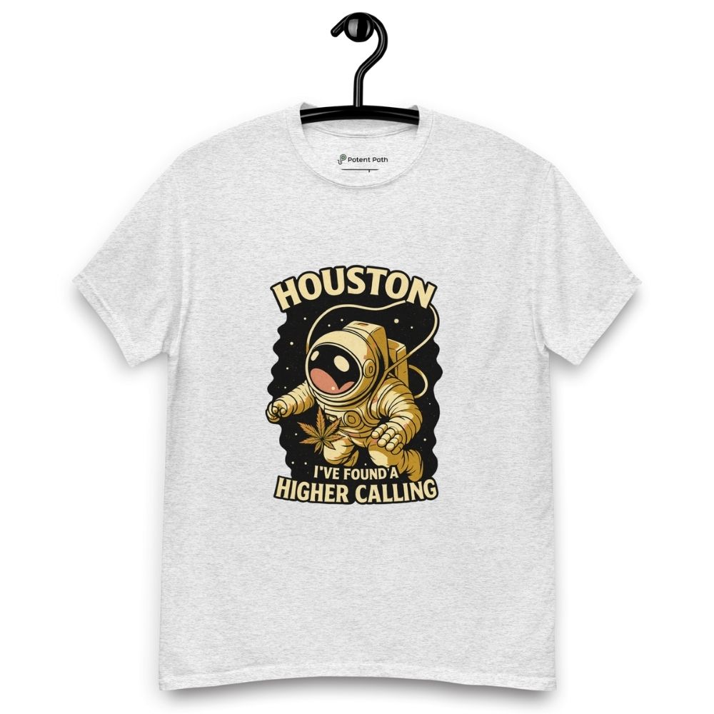 Grey t-shirt on a hanger featuring a cartoon astronaut holding a cannabis leaf, surrounded by stars, with the text "HOUSTON I'VE FOUND A HIGHER CALLING”