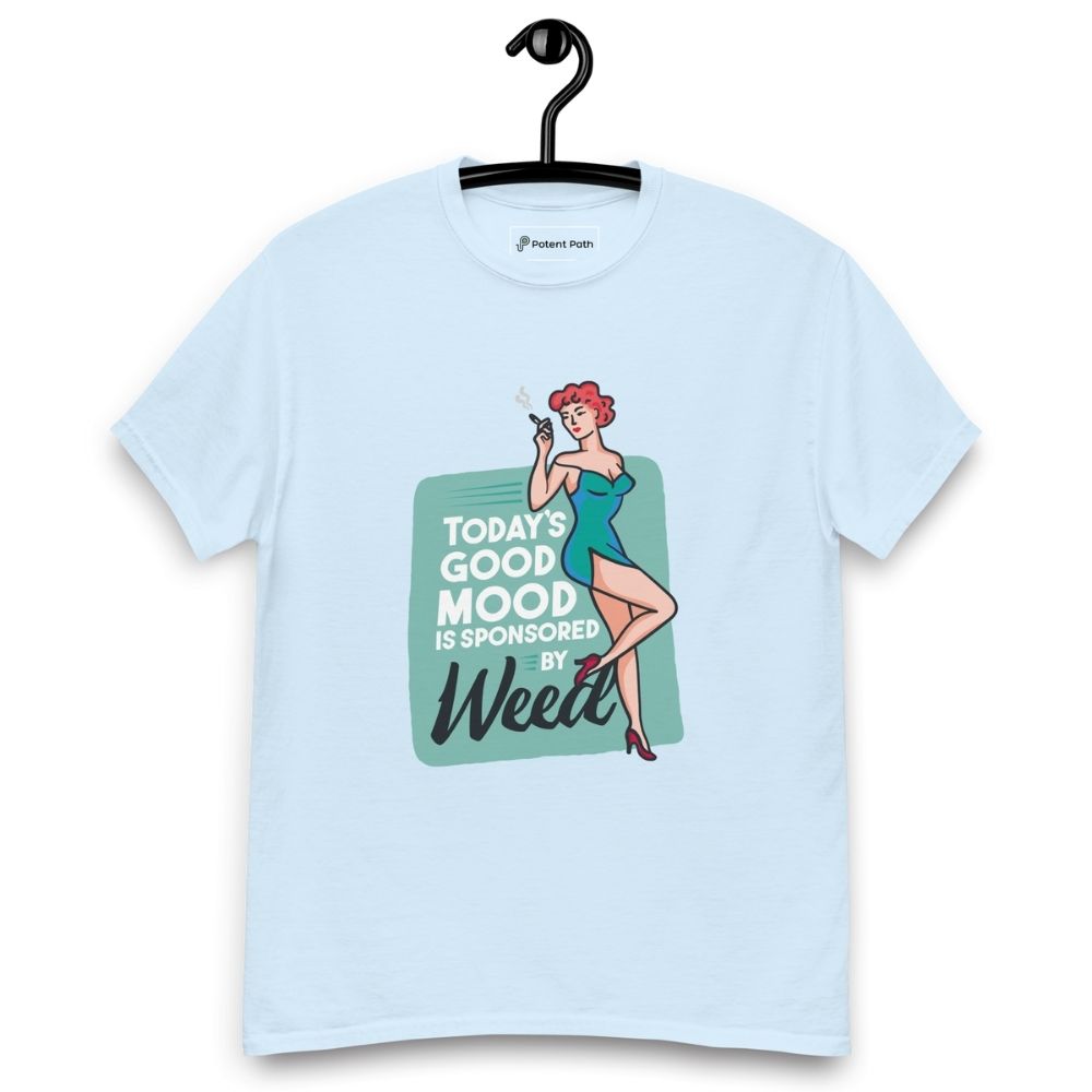 Light blue T-shirt on a hanger featuring a retro-style illustration of a woman in a teal dress holding a smoking joint, next to the text “TODAY'S GOOD MOOD IS SPONSORED BY Weed"