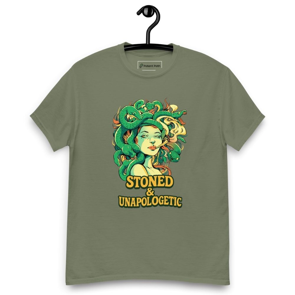 Military green T-shirt on a hanger featuring a Medusa head smoking a joint with green snake hair, and the text "STONED & UNAPOLOGETIC" below