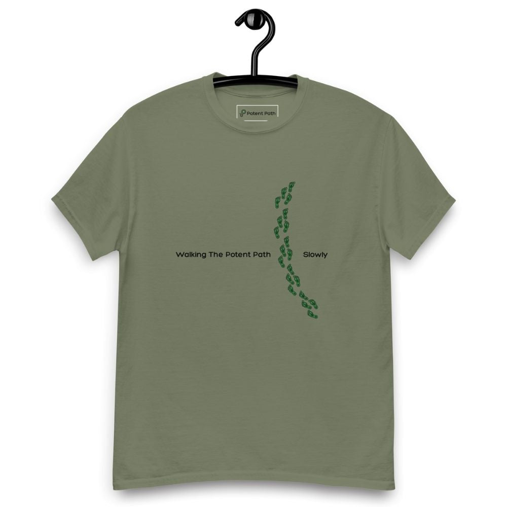 Military green t-shirt on a hanger featuring the phrase "Walking The Potent Path Slowly" in white text across the chest, with a vertical trail of small green footprints with cannabis leaves inside between "Path" and "Slowly"