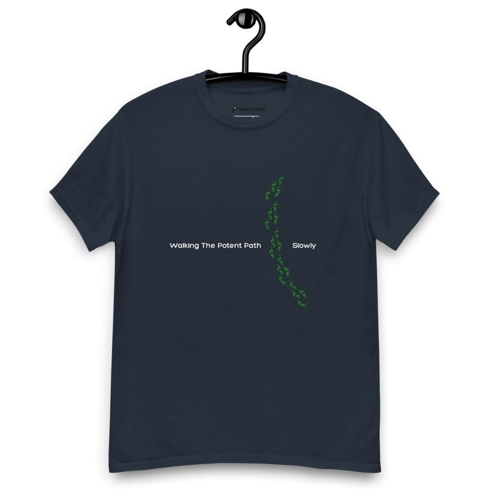 Navy blue t-shirt on a hanger featuring the phrase "Walking The Potent Path Slowly" in white text across the chest, with a vertical trail of small green footprints with cannabis leaves inside between "Path" and "Slowly"
