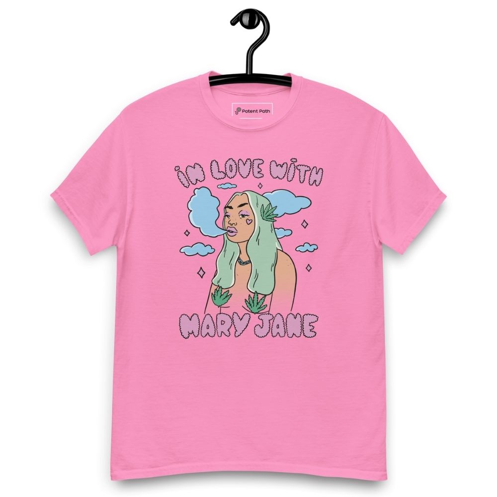 Pink T-shirt on a hanger featuring a cartoon woman with long green hair, cannabis leaves covering her breasts and smoke clouds behind her, with the text "IN LOVE WITH MARY JANE" above and "MARY JANE" below the illustration