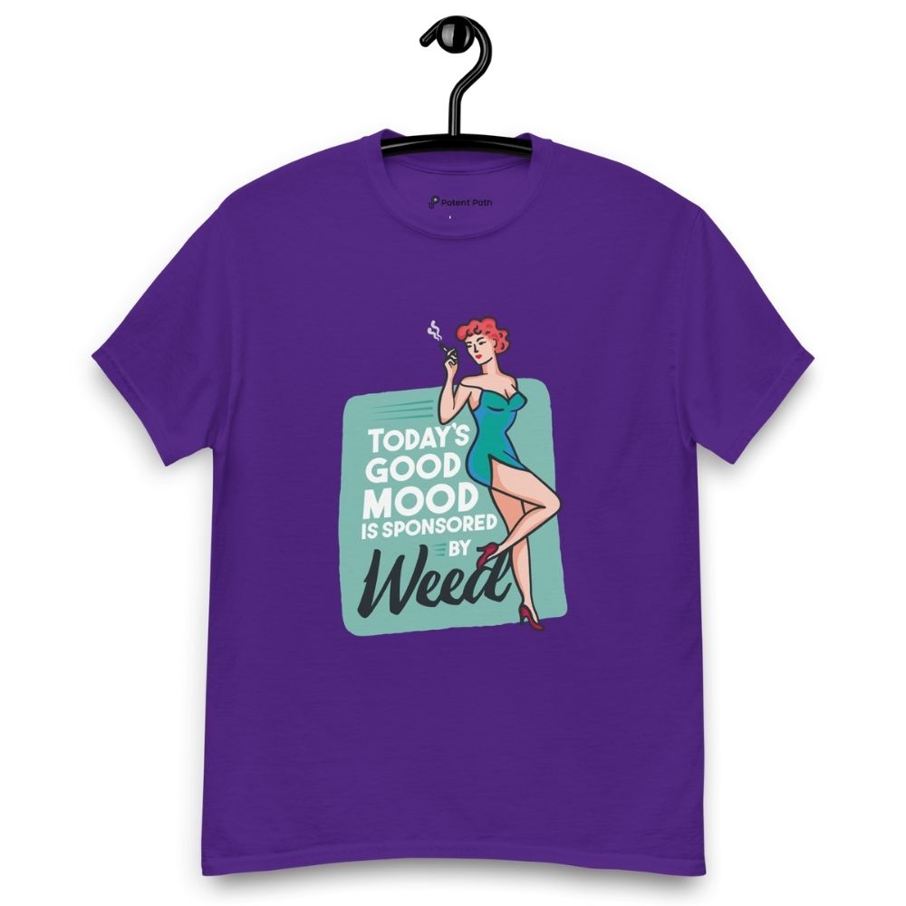 Purple T-shirt on a hanger featuring a retro-style illustration of a woman in a teal dress holding a smoking joint, next to the text “TODAY'S GOOD MOOD IS SPONSORED BY Weed"