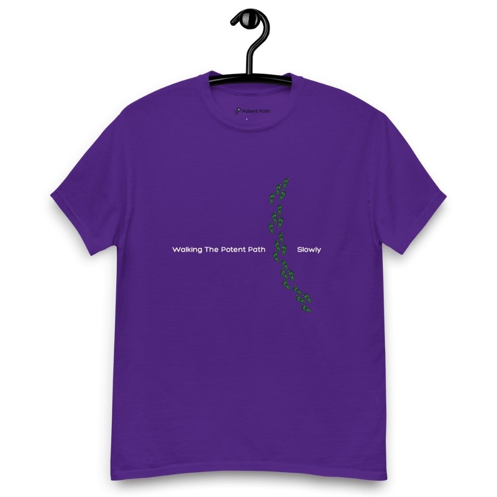 Purple t-shirt on a hanger featuring the phrase "Walking The Potent Path Slowly" in white text across the chest, with a vertical trail of small green footprints with cannabis leaves inside between "Path" and "Slowly"