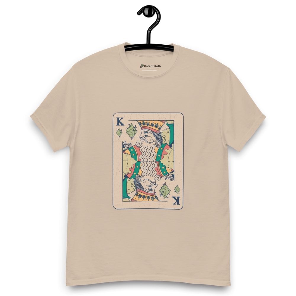 A sandy colour T-shirt on a hanger featuring a vintage-style playing card design of the King holding a weed joint, with the suit replaced by cannabis leaves