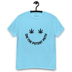 Sky blue t-shirt on a hanger featuring curved text reading "ON THE POTENT PATH" in the form of a smiley face and two black cannabis leaves above to represent the eyes