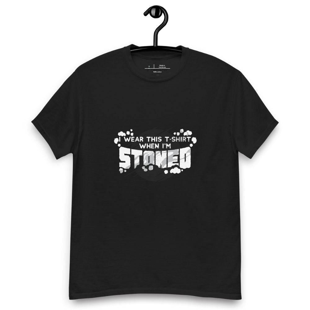 Black T-shirt on a hanger with a graphic on the chest area that has a text surrounded by small cloud puffs that reads, "I WEAR THIS T-SHIRT WHEN I'M STONED"