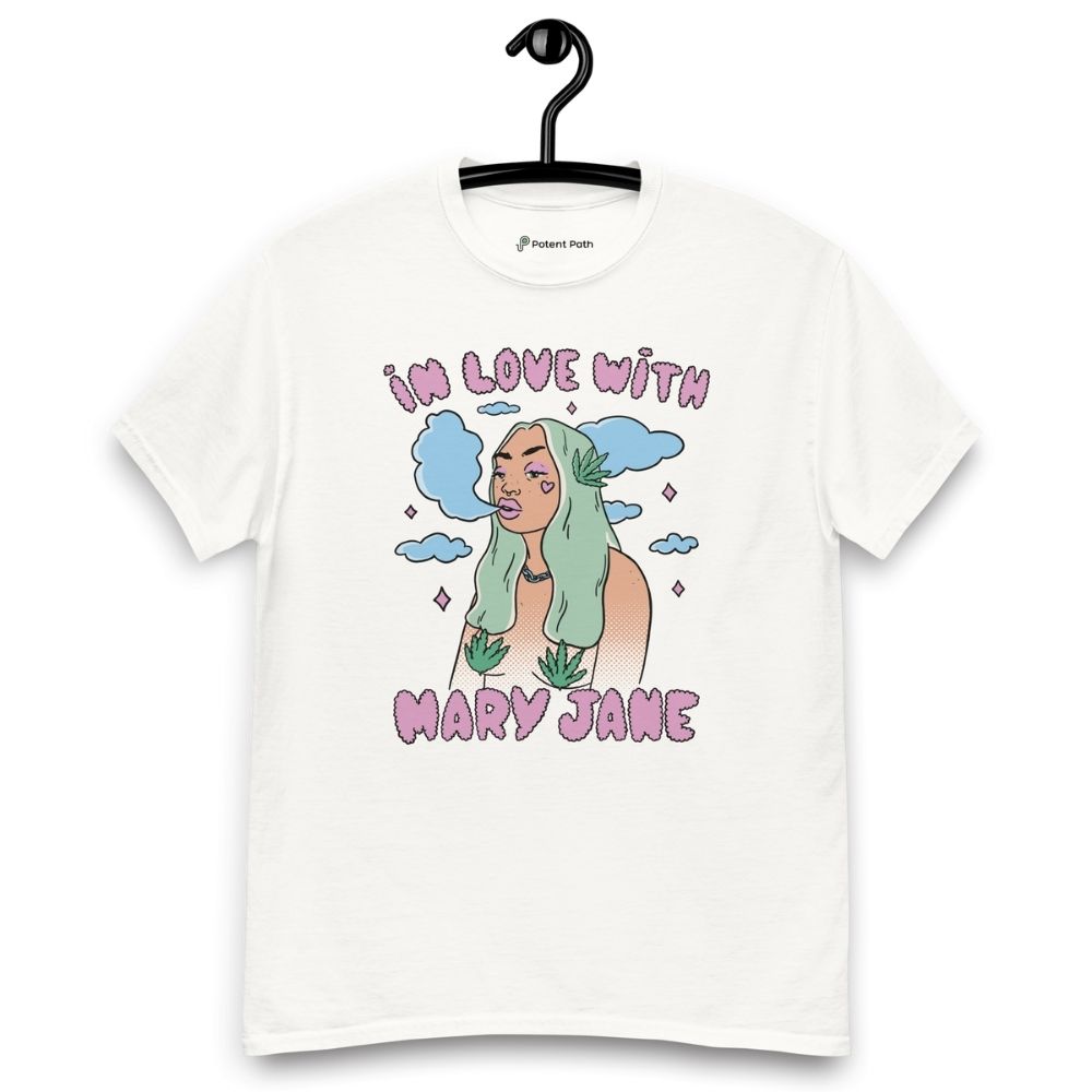 White T-shirt on a hanger featuring a cartoon woman with long green hair, cannabis leaves covering her breasts and smoke clouds behind her, with the text "IN LOVE WITH MARY JANE" above and "MARY JANE" below the illustration.