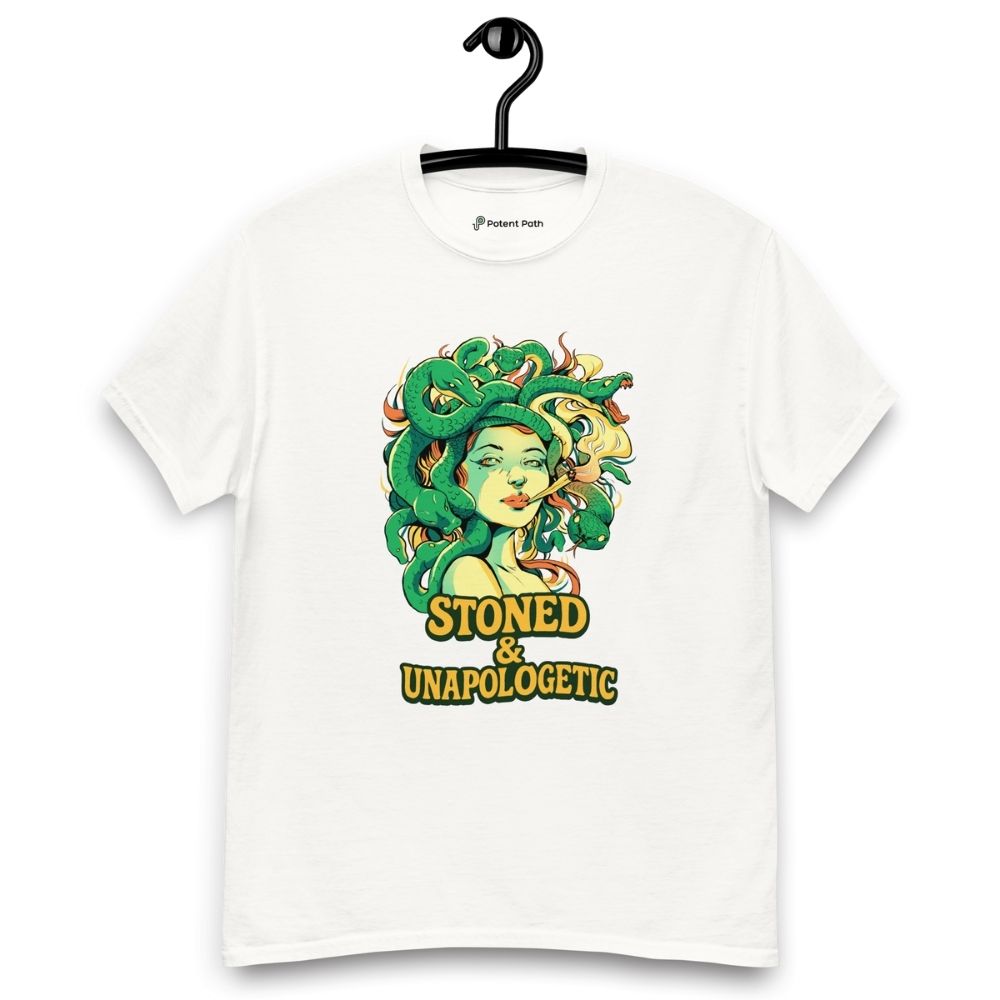 White T-shirt on a hanger featuring a Medusa head smoking a joint with green snake hair, and the text "STONED & UNAPOLOGETIC" below