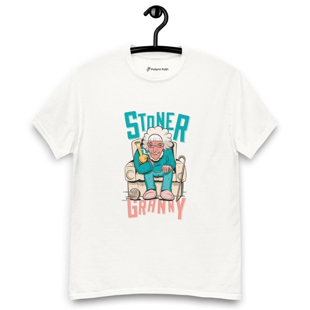 White T-shirt on a hanger featuring a cartoon illustration of an elderly woman in a teal tracksuit sitting in an armchair, holding a yellow bong, with the text "STONER GRANNY" above and below her.