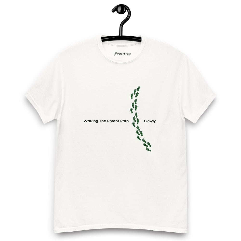 White t-shirt on a hanger featuring the phrase "Walking The Potent Path Slowly" in white text across the chest, with a vertical trail of small green footprints with cannabis leaves inside between "Path" and "Slowly"